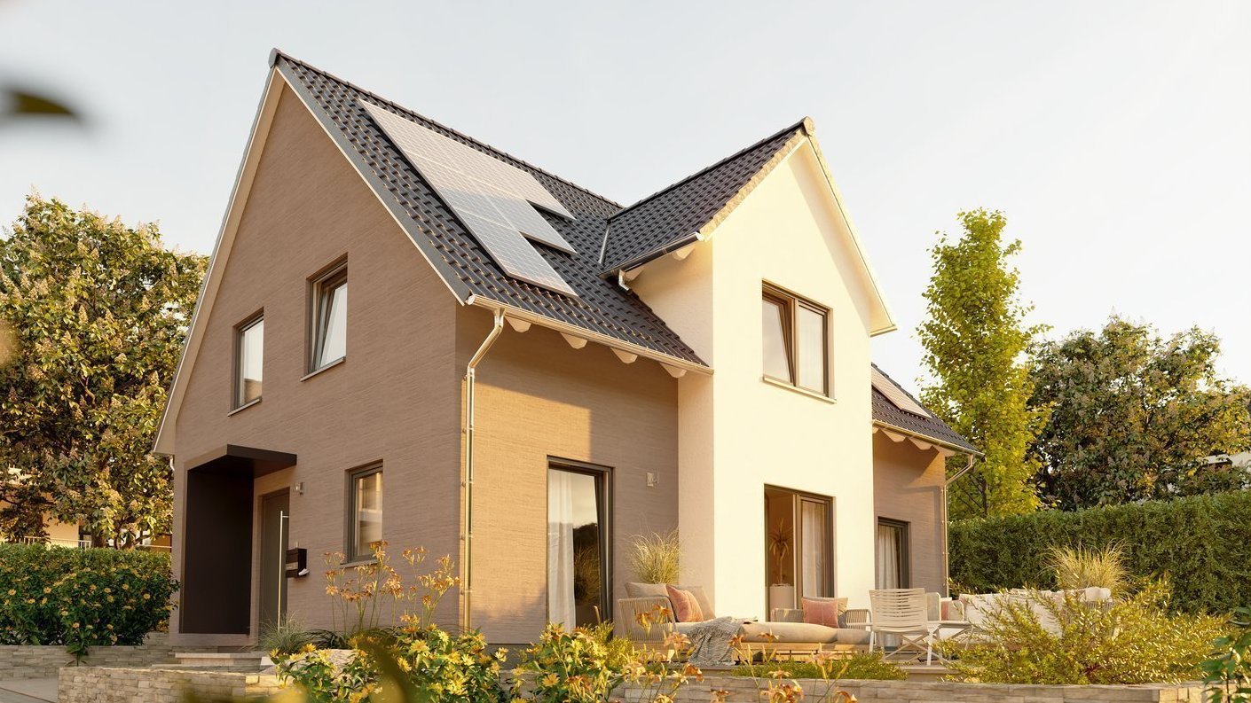 Modernes Einfamilienhaus mit Terrasse und Solarmodulen auf dem Satteldach in einem gepflegten Garten bei Abendlicht.