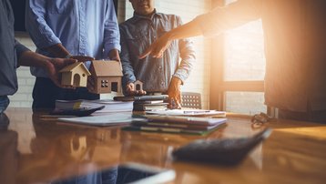Beratungsgespräch zur Hausplanung mit Hausmodell, Unterlagen und Taschenrechner