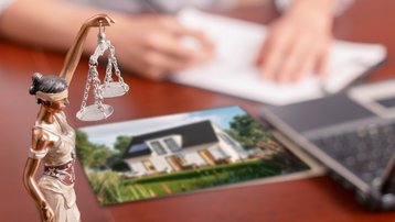 Justitia-Figur neben Hausbild, Laptop und Unterlagen zur rechtlichen Planung beim Hausbau