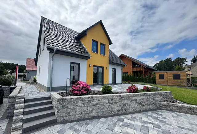 Modernes Einfamilienhaus von Thielker MassivHaus mit heller Putzfassade, gelbem Fassadenakzent, großzügiger Terrasse und gepflegter Außenanlage im Münsterland.