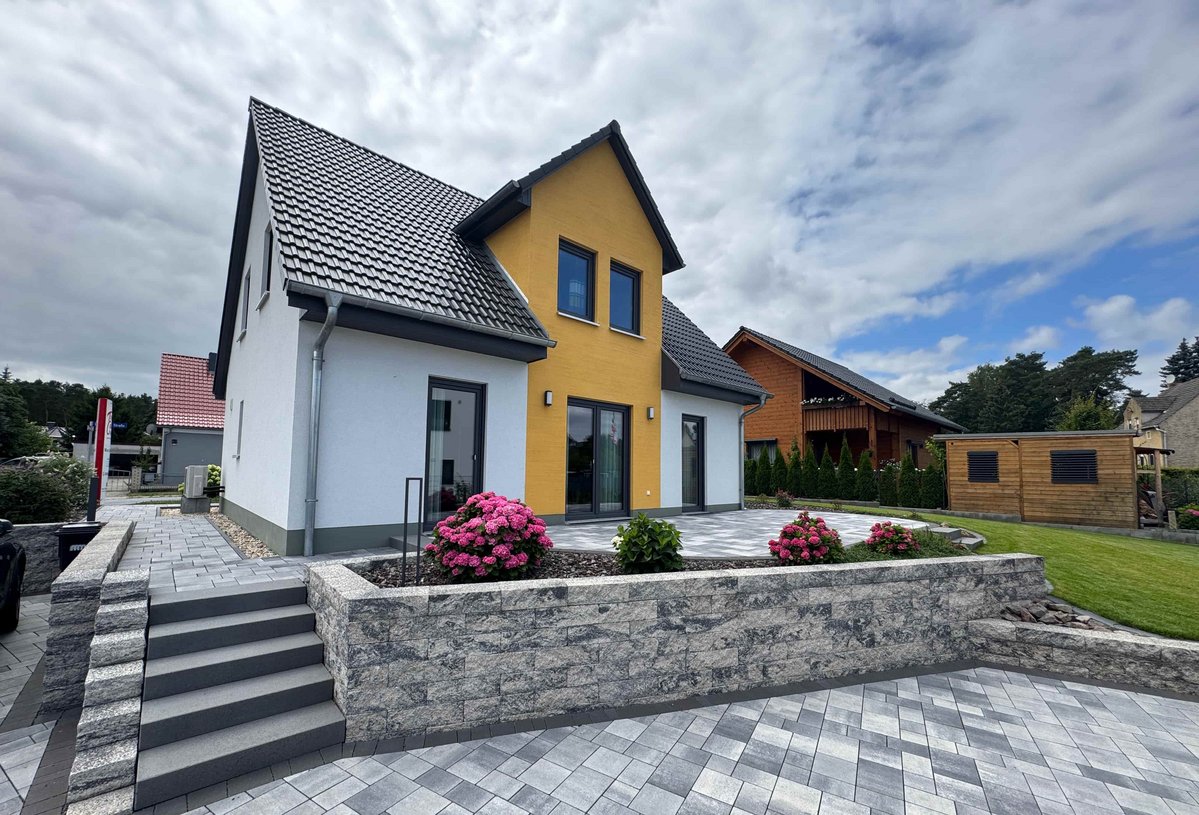 Modernes Einfamilienhaus von Thielker MassivHaus mit heller Putzfassade, gelbem Fassadenakzent, großzügiger Terrasse und gepflegter Außenanlage im Münsterland.