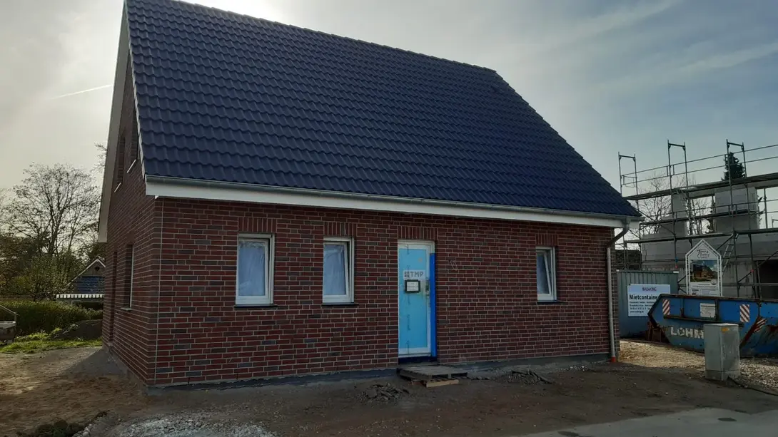 Klinkerhaus im Baugebiet kurz vor Fertigstellung Einfamilienhaus mit roter Klinkerfassade, dunklem Satteldach und Baustellenbereich im Vordergrund