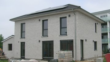 Neubau eines zweigeschossigen Einfamilienhauses aus hellem Klinker mit Walmdach und Photovoltaikanlage.