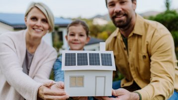 Familie hält ein Hausmodell mit Solaranlage als Symbol für nachhaltigen Hausbau