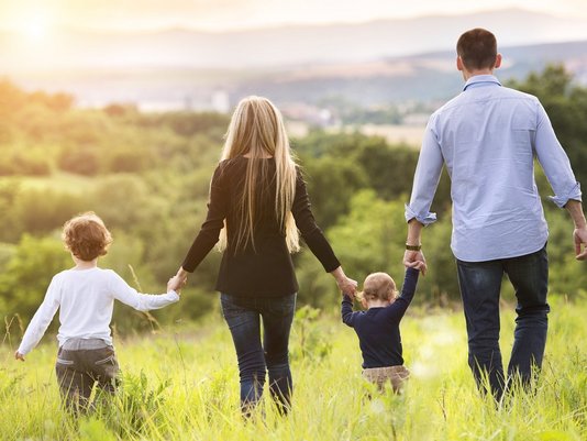 Familie mit zwei Kindern läuft Hand in Hand über eine Wiese – Symbolbild für Familienleben im eigenen Haus.