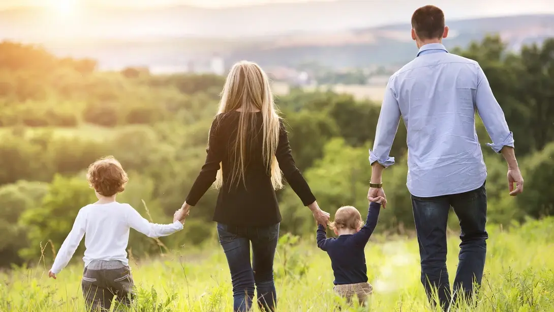 Familie in grüner Natur bei Sonnenuntergang Familie mit zwei Kindern geht bei Sonnenuntergang durch eine grüne Landschaft