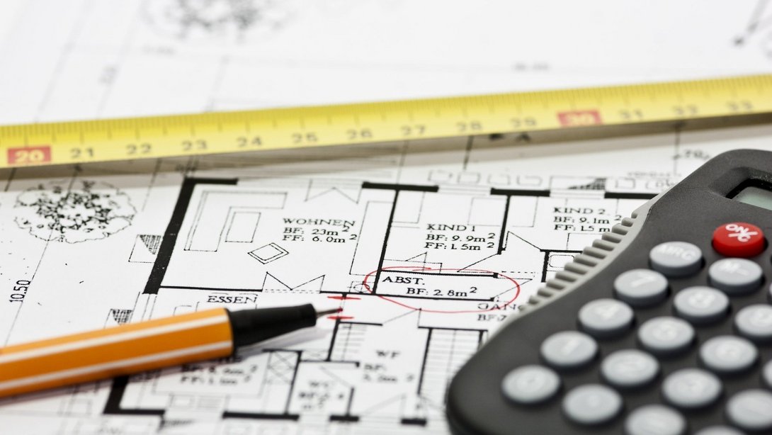 Hausgrundriss auf Bauplan mit Zollstock, Stift und Taschenrechner zur Planung eines Hausbaus