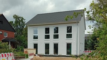 Neubau eines zweigeschossigen Einfamilienhauses mit grauem Satteldach; davor Baustellenabsperrungen und unbefestigter Vorgarten.