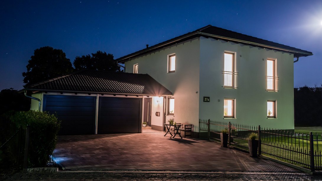 Modernes Einfamilienhaus mit Garage und beleuchteten Fenstern bei Nacht – Massivhaus von Thielker MassivHaus