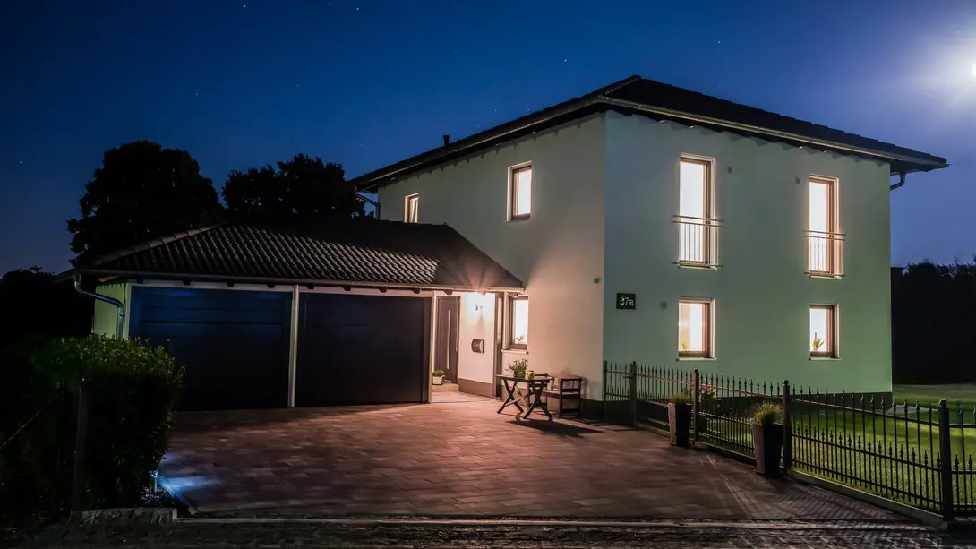 Modernes Einfamilienhaus mit Garage – Thielker MassivHaus Modernes Einfamilienhaus mit Garage und beleuchteten Fenstern bei Nacht – Massivhaus von Thielker MassivHaus
