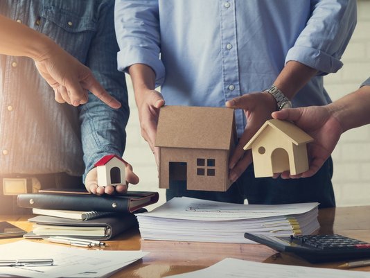 Personen planen ein Hausprojekt mit Modellhaus, Bauplänen und Taschenrechner – Symbolbild für Bauplanung und Finanzierung.