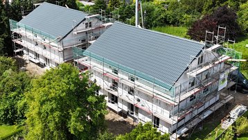 Luftaufnahme von zwei Neubauten mit Baugerüsten und grauen Satteldächern in einem Wohngebiet.