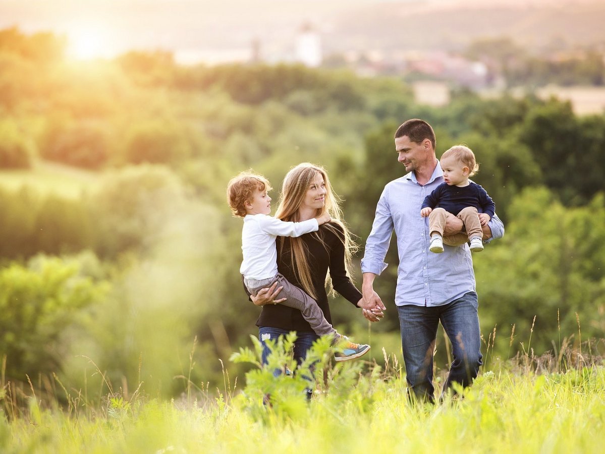 Familie in grüner Natur bei Abendlicht Familie mit zwei Kindern steht bei Sonnenuntergang in einer grünen Landschaft