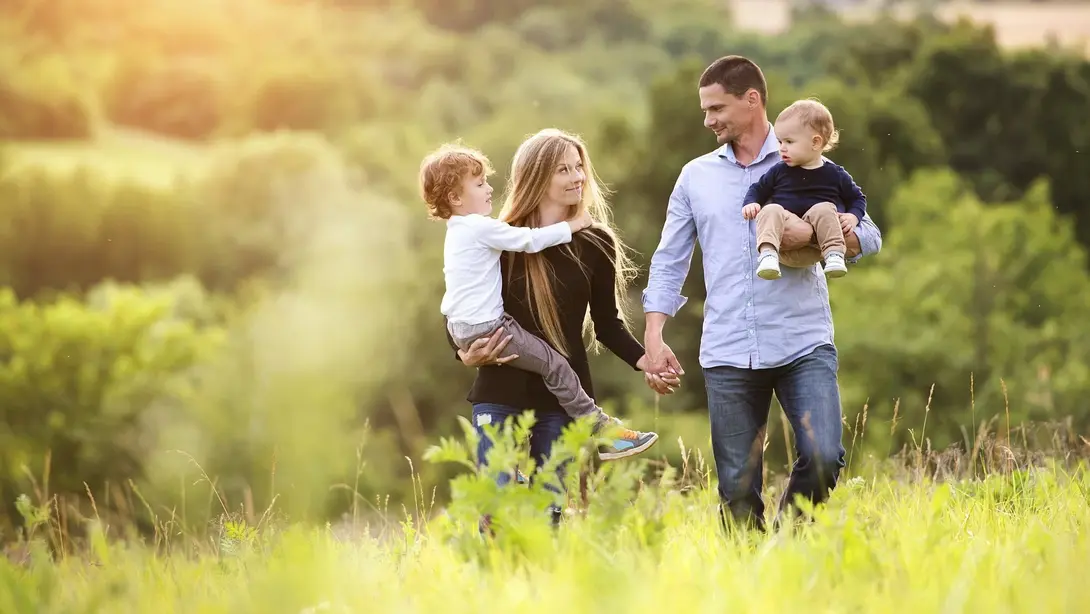 Familie mit zwei Kindern spaziert bei Sonnenuntergang durch eine grüne Landschaft
