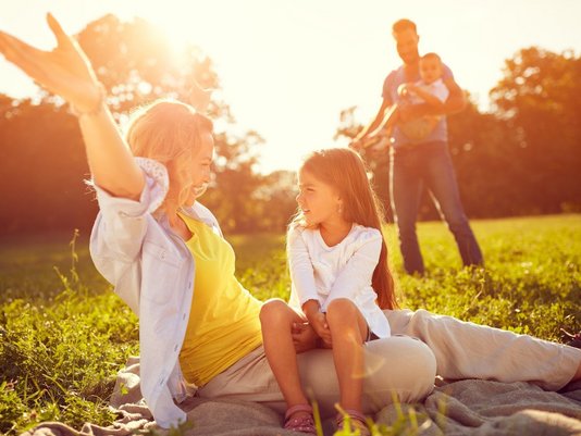 Familie entspannt auf einer Wiese im Sonnenlicht – Eltern und Kind genießen gemeinsame Zeit im Grünen.