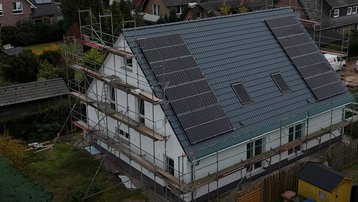 Luftaufnahme eines Einfamilienhauses mit Baugerüst und Photovoltaikanlage auf dem Satteldach in einem Wohngebiet.