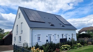 Modernes Einfamilienhaus mit Photovoltaikanlage auf dem Satteldach und gepflegtem Garten.