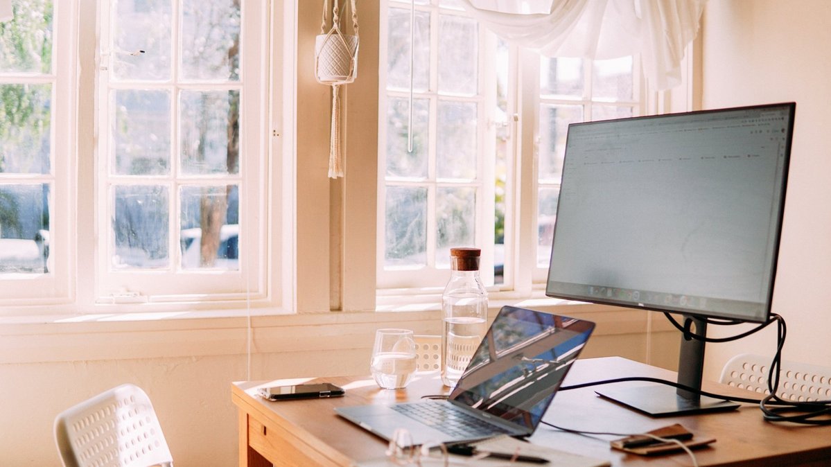 Heller Arbeitsplatz im Homeoffice mit Laptop, Monitor und Fensterblick