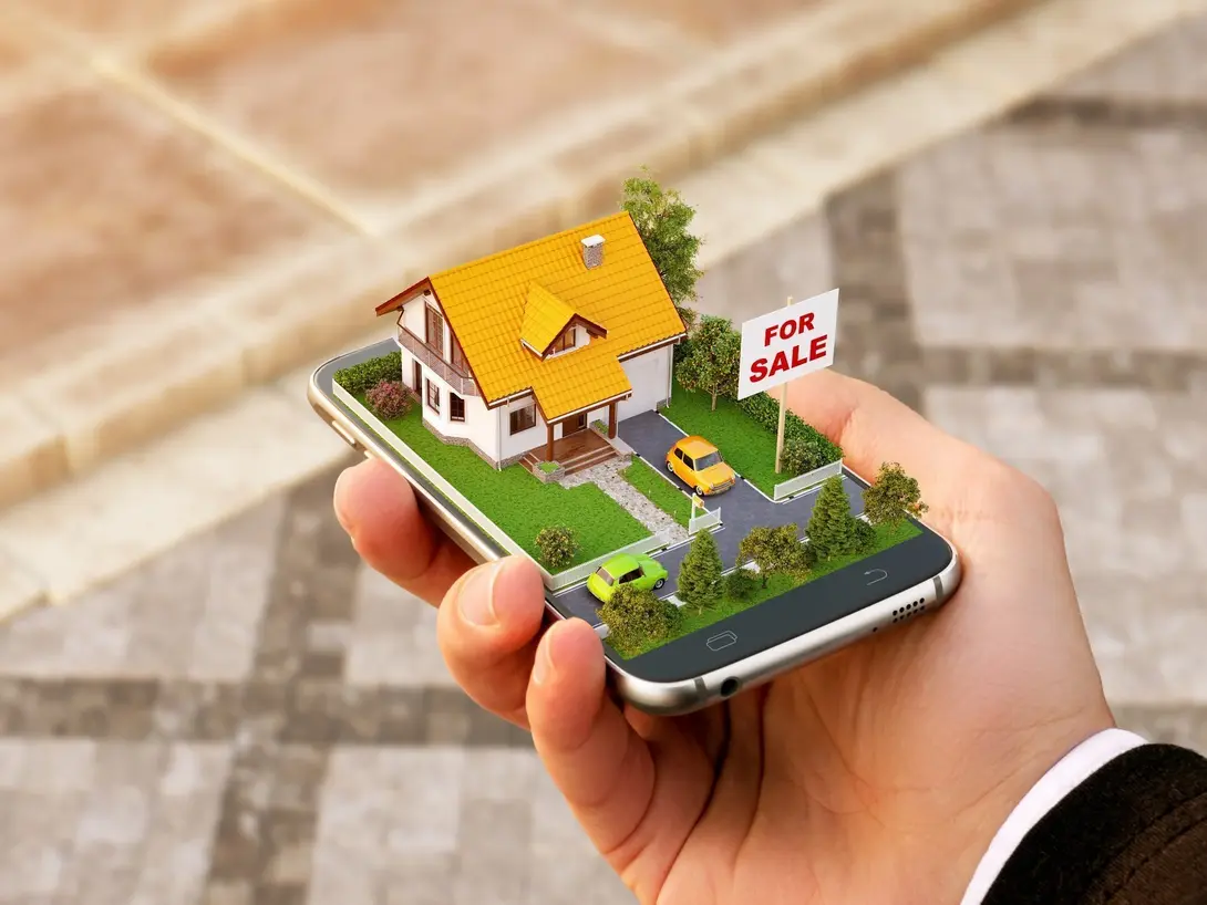 Hausplanung und Grundstückssuche digital vorbereiten Smartphone mit digitalem Hausmodell und Immobilien-Symbolen in der Hand – Symbolbild für Hausplanung und Grundstückssuche.
