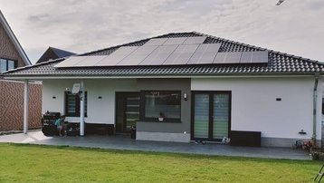 Moderner Bungalow mit Photovoltaikanlage auf dem Dach und großer Rasenfläche im Vordergrund.