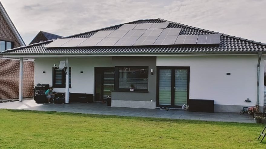 Energieeffizienter Bungalow in Steinfurt Moderner Bungalow mit Photovoltaikanlage auf dem Dach und großer Rasenfläche im Vordergrund.
