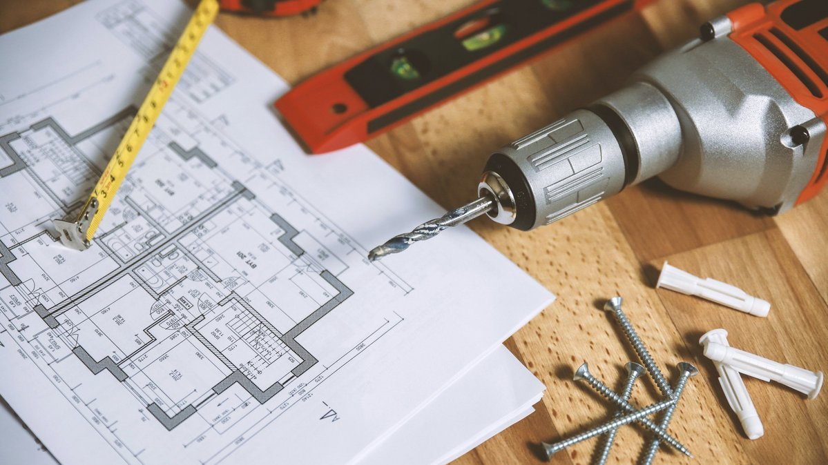 Bauplan mit Maßband, Bohrmaschine, Schrauben und Wasserwaage auf einer Holzfläche