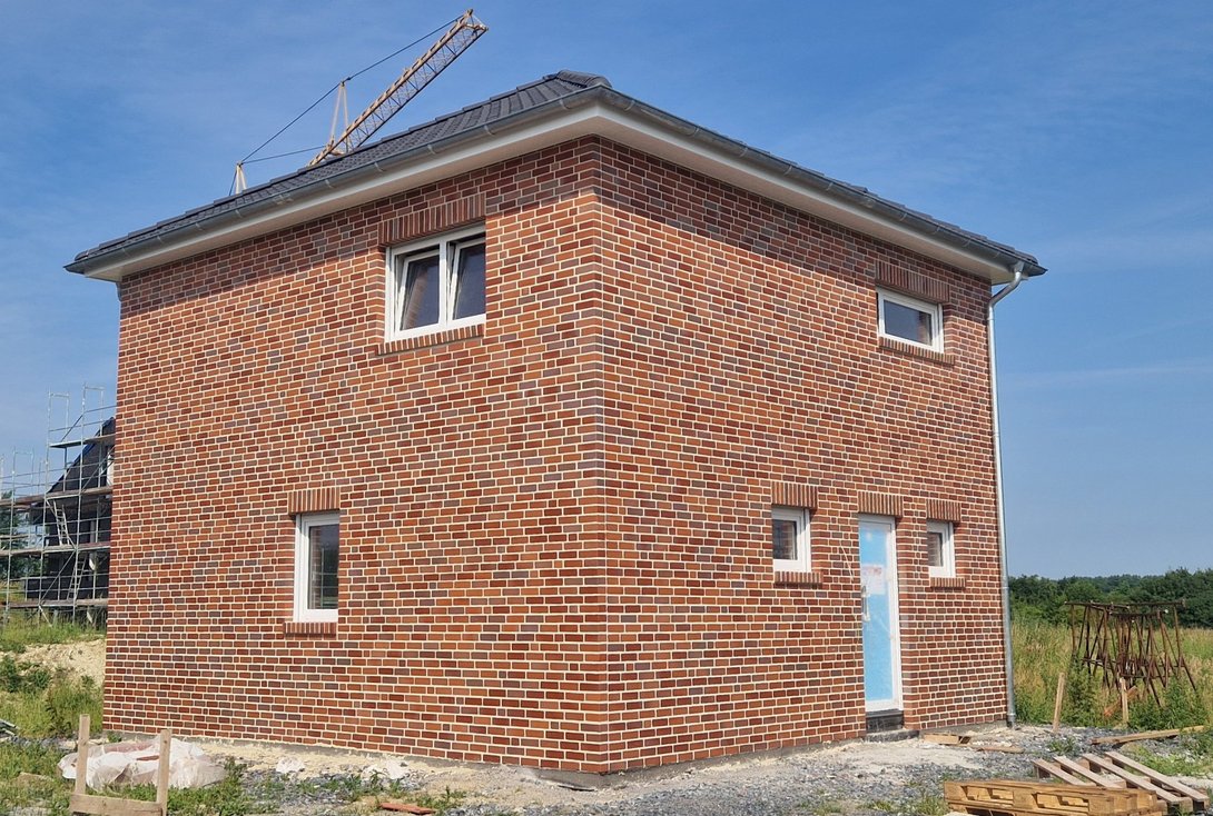 Massivhaus-Neubau mit roter Klinkerfassade und Walmdach während der Bauphase