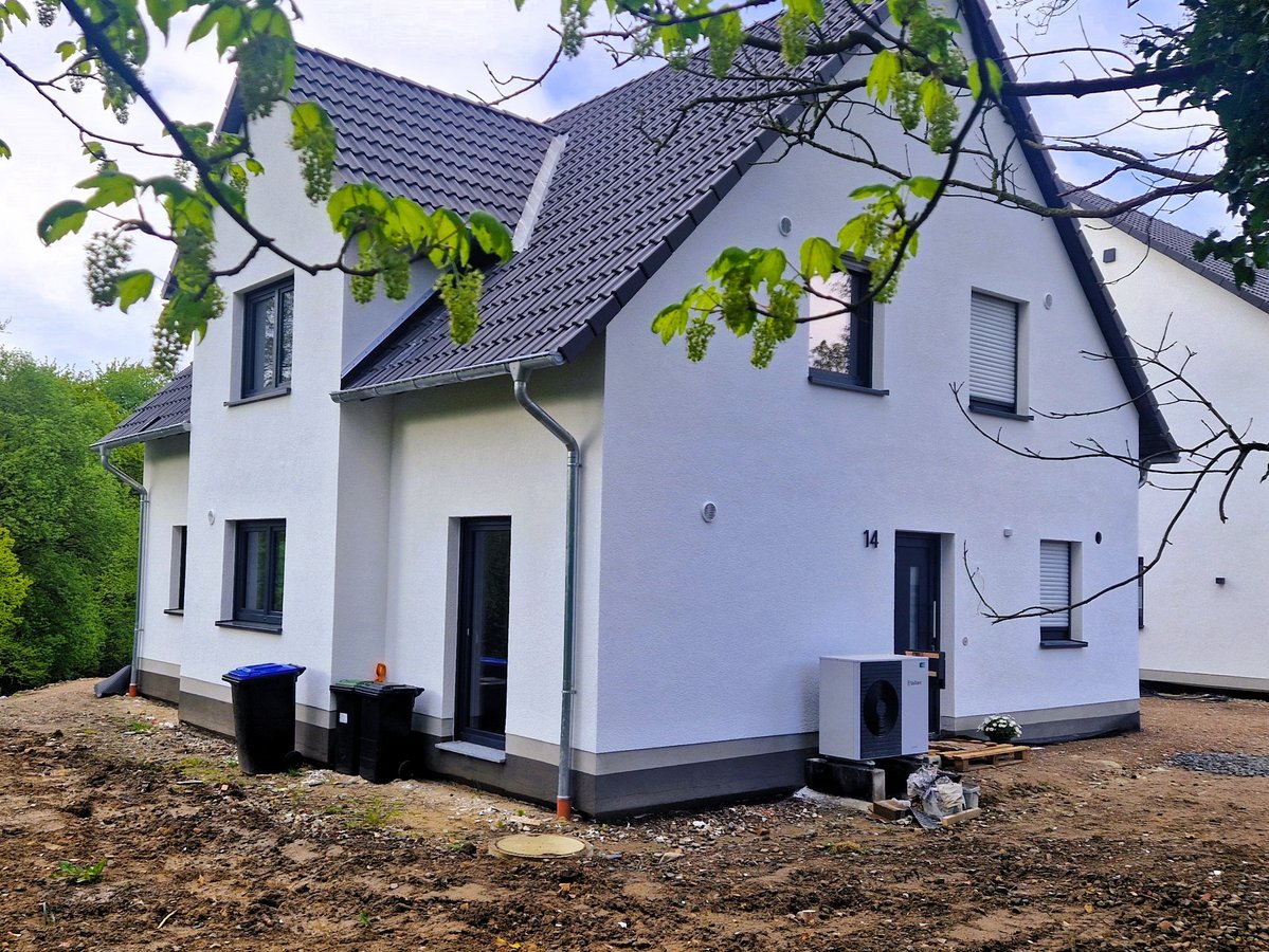 Außenansicht eines weißen Einfamilienhauses mit Satteldach, Bäumen im Vordergrund.