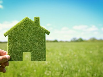 Nachhaltig bauen mit grünem Hauskonzept Grünes Haus-Symbol aus Gras in einer Hand vor unscharfer Wiese als Symbol für nachhaltiges Bauen
