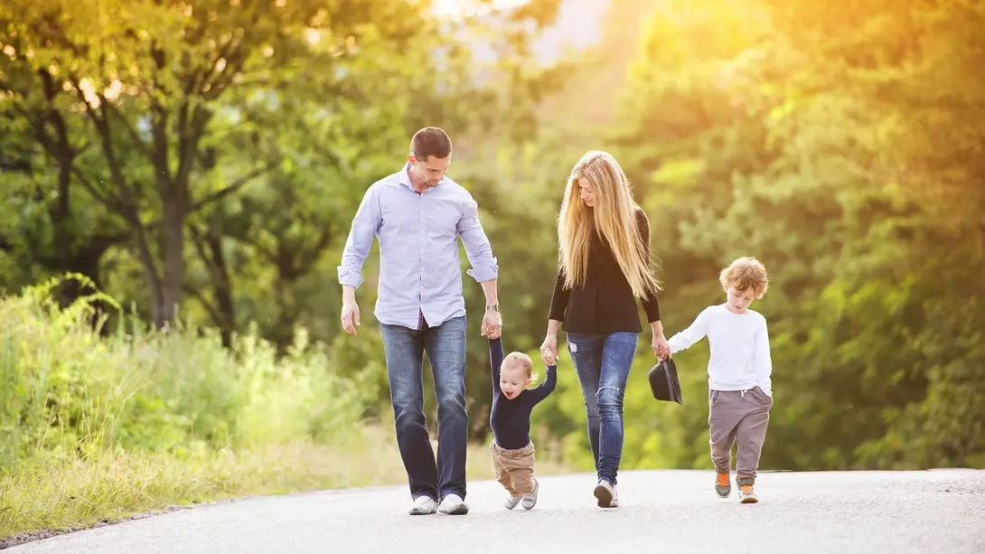 Familie mit zwei Kindern geht bei Sonnenlicht auf einem Weg durch eine grüne Naturumgebung