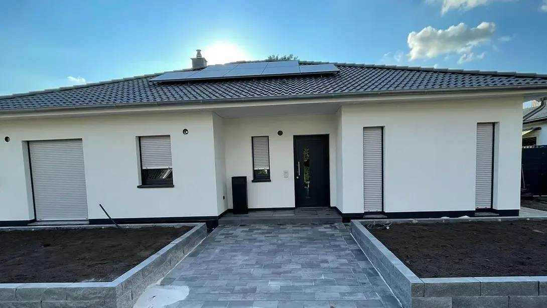 Moderner Bungalow mit weißer Fassade, Walmdach, Photovoltaikanlage und gepflastertem Eingangsbereich