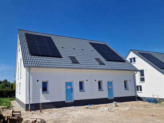 Neubau mit Photovoltaik-Anlage auf Satteldach Neubau-Einfamilienhaus mit Photovoltaikanlage auf dem Dach bei sonnigem Himmel.