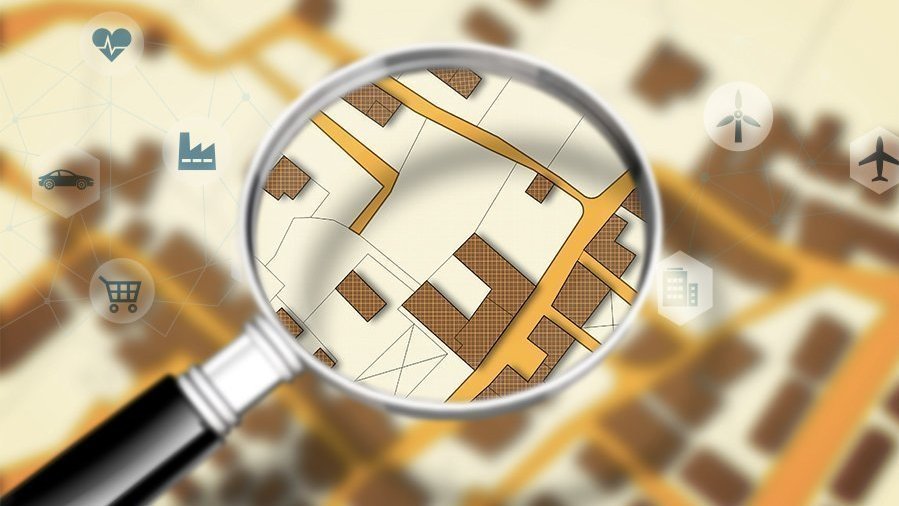 Lupe über einem Lageplan mit Infrastruktur-Symbolen zur Standortanalyse beim Hausbau